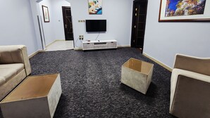 Una habitación con televisión de pantalla plana, un mueble blanco de entretenimiento, un cuadro enmarcado y piso alfombrado.