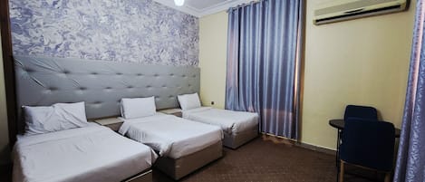 Ett hotellrum med två separata sängar, ett litet skrivbord, en stol, en vägg med mönster och en taklampa.
