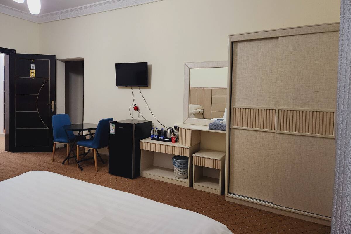 A hotel room with a bed, a desk with a computer, a TV, a wardrobe, and a bathroom.
