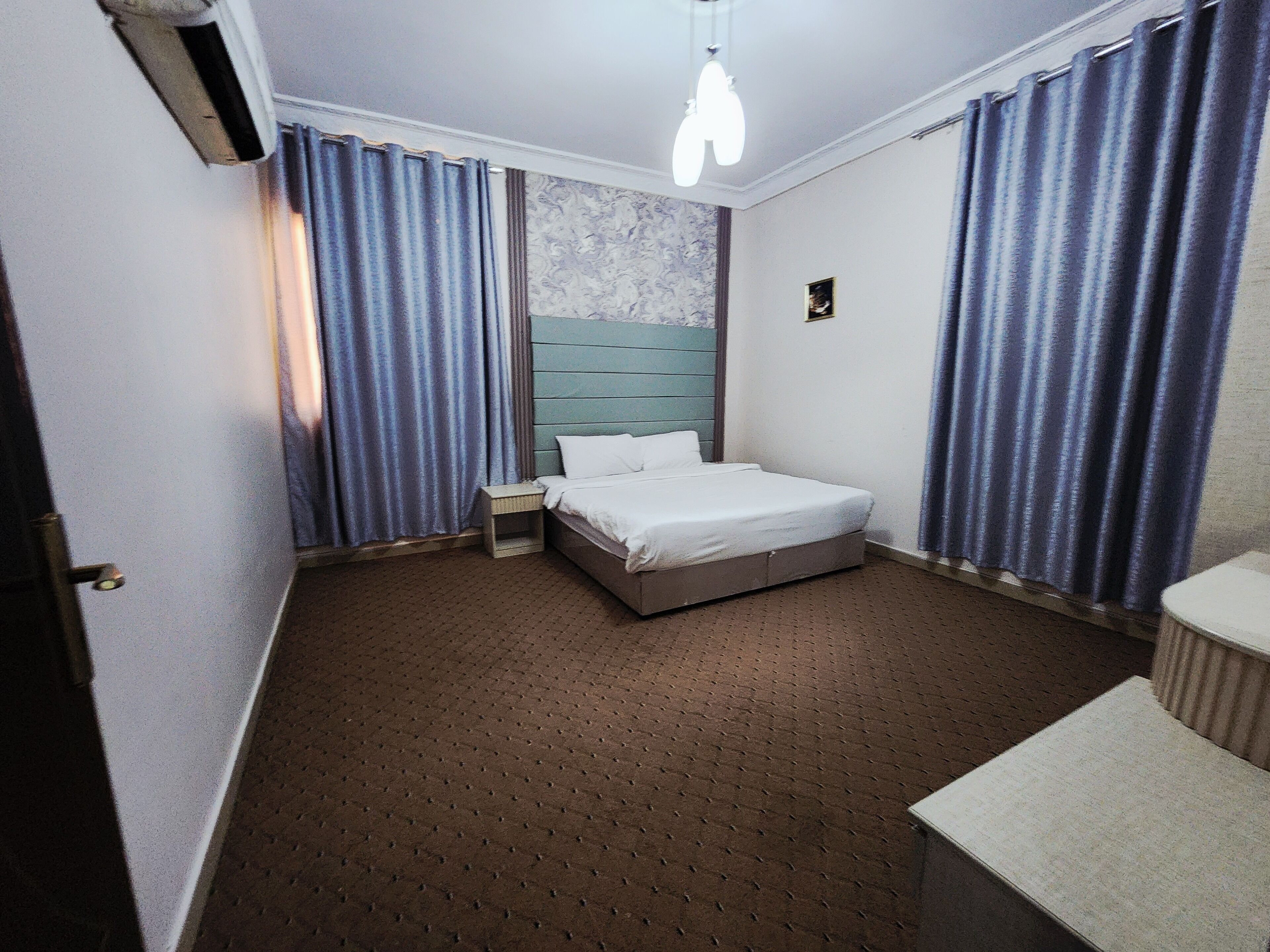 A hotel room with a bed, a nightstand, a small table, and a window with curtains.