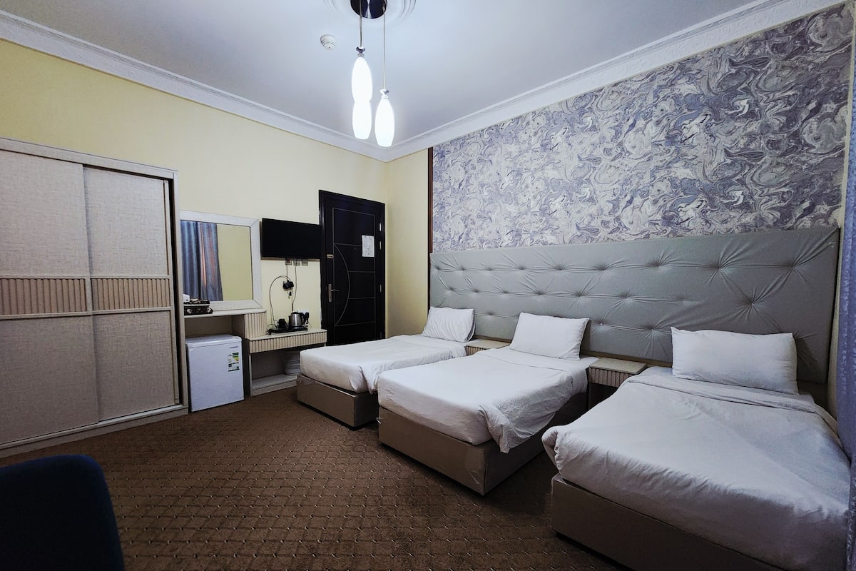 A hotel room with two beds, a desk with a chair, a wardrobe, and a bathroom.