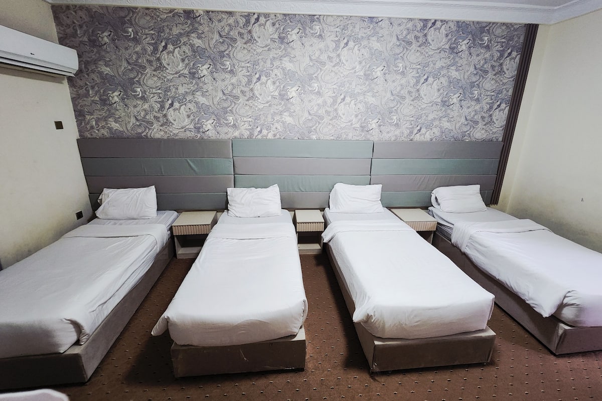 A hotel room with four single beds arranged in a row, a marble-patterned wall, and a grey headboard.