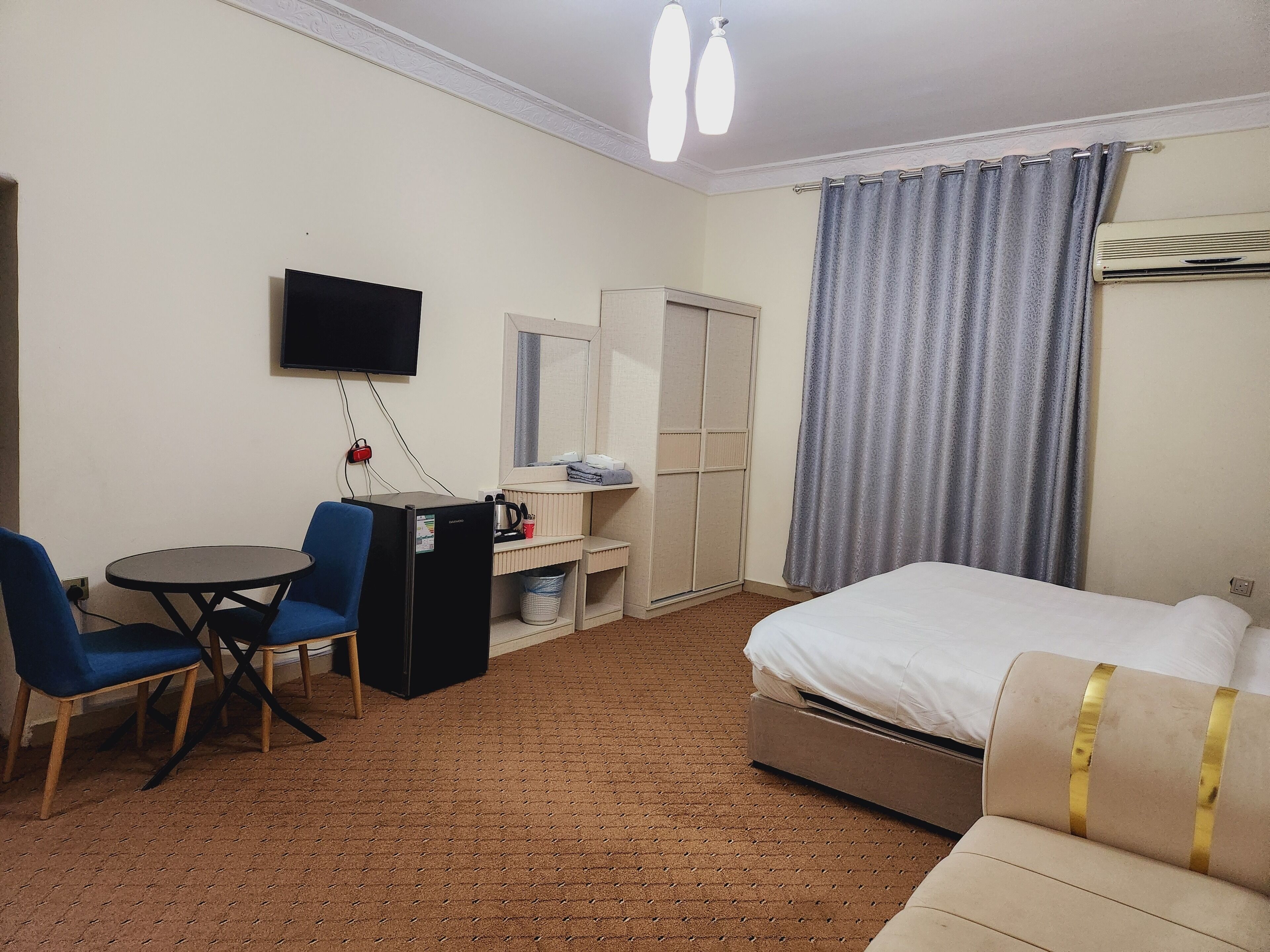 A hotel room with a bed, a desk with a chair, a television, a wardrobe, and a window with curtains.