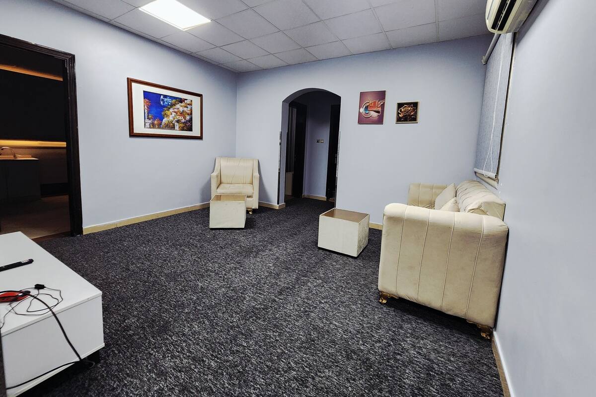 A conference room with a carpeted floor, a white desk, a beige armchair, and a sofa.