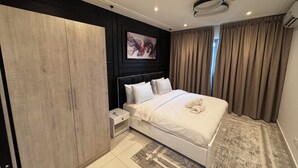 A modern hotel room with a large bed, a wooden wardrobe, a small bedside table, and a painting on the wall. - Loxwood Abode (Accra)