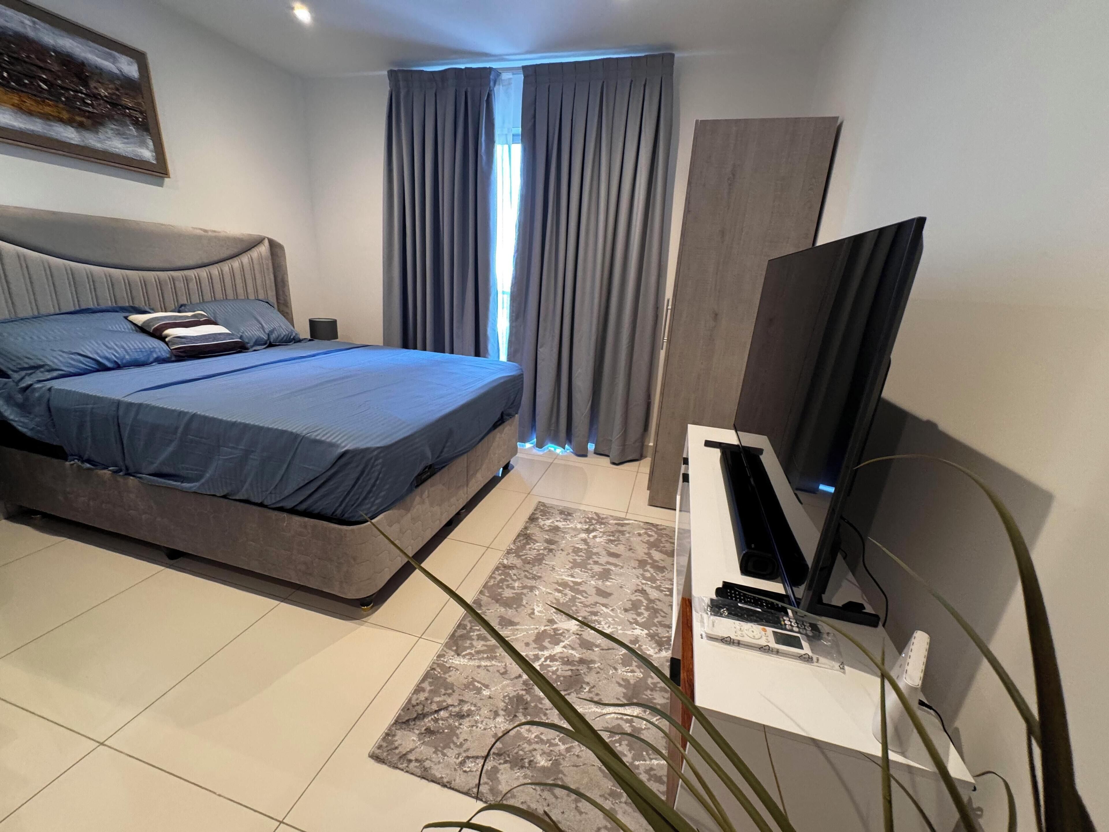 Een moderne slaapkamer met een bed, een televisie op een standaard en een raam met gordijnen.