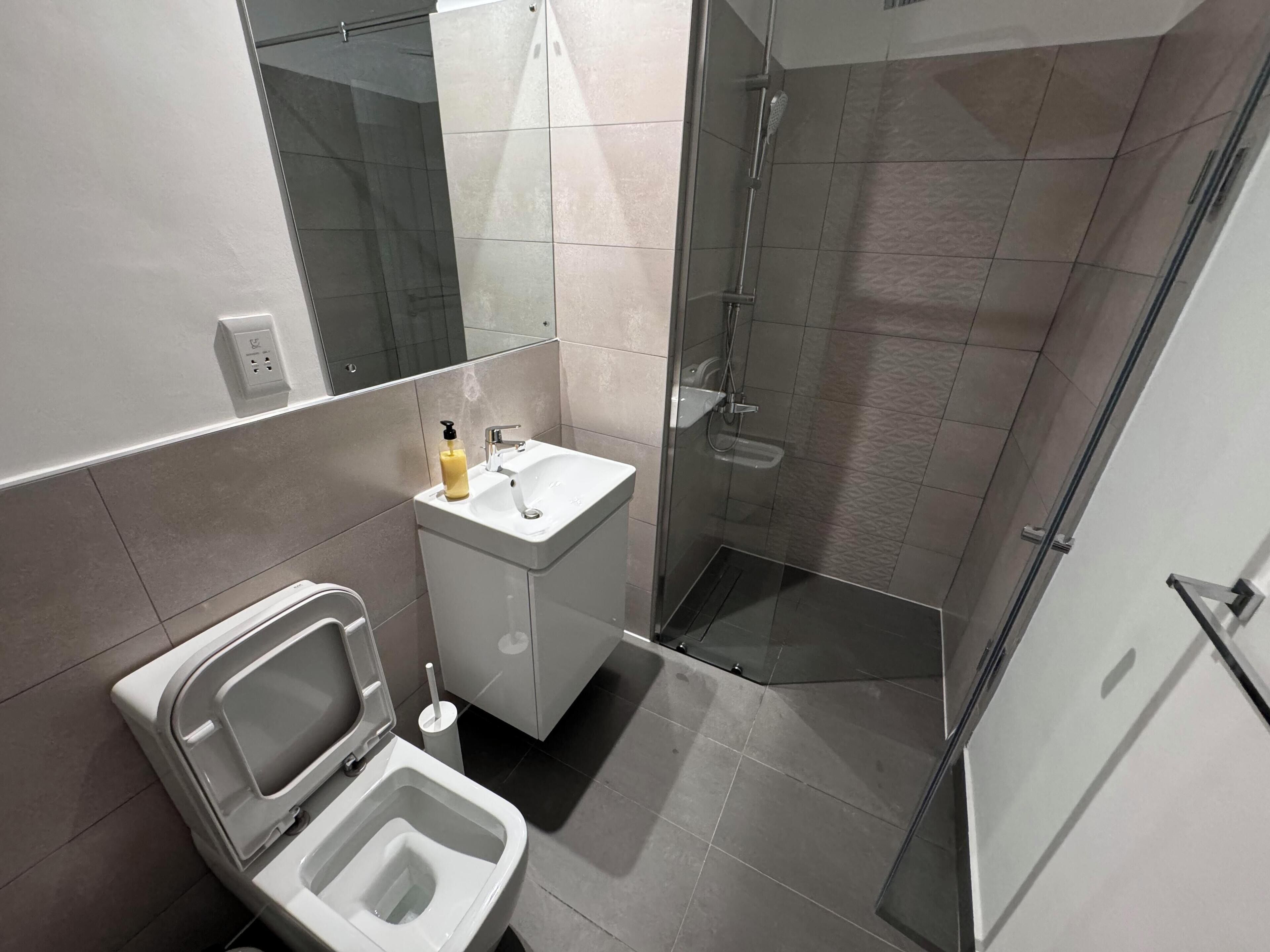 Et stilfuldt badeværelse med toilet, vask og brusebad med glasvægge.