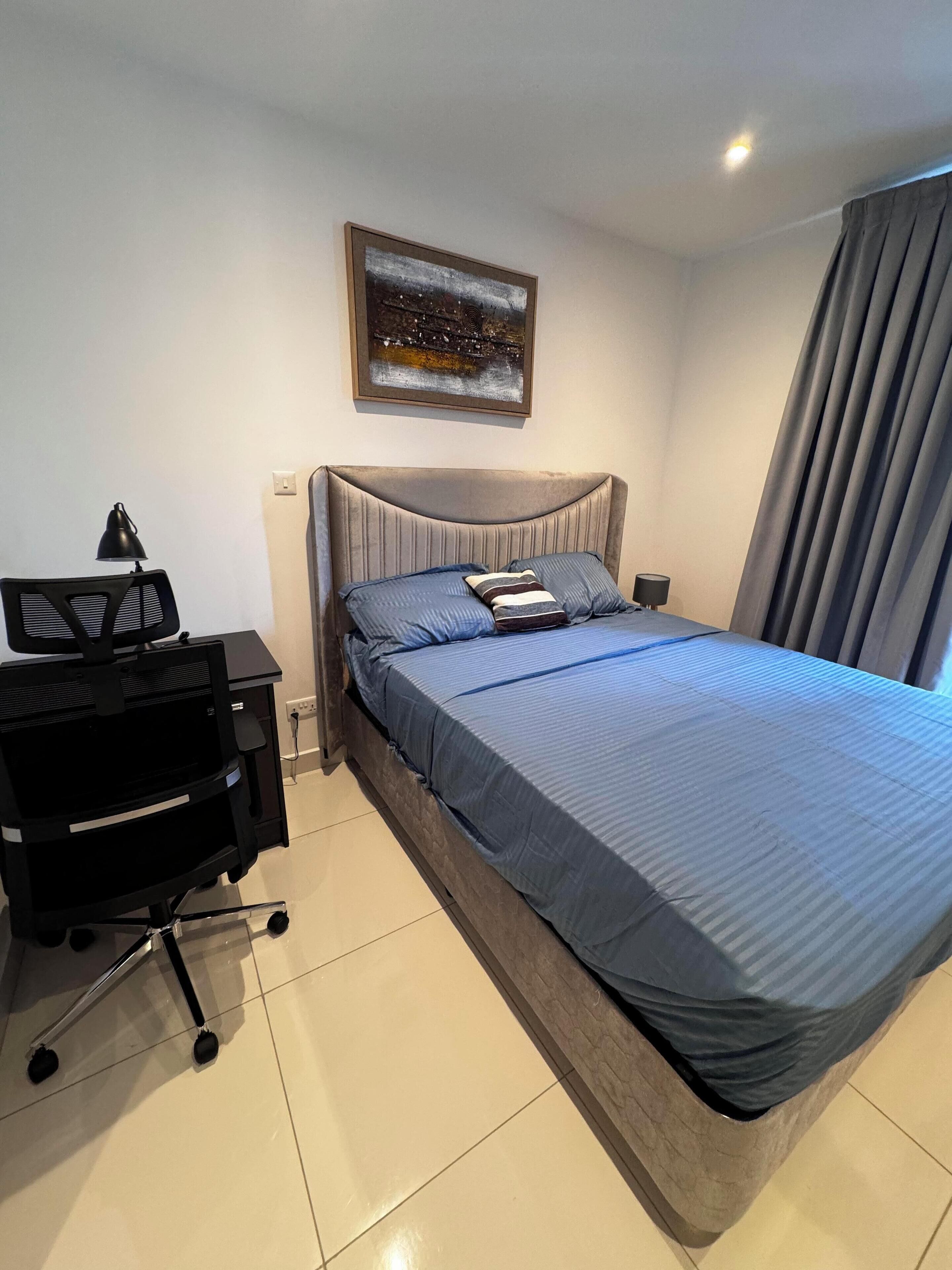 A hotel room with a large bed, a desk with a chair, a lamp, and a painting on the wall.