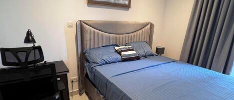A hotel room with a large bed, a desk with a chair, a lamp, and a painting on the wall.