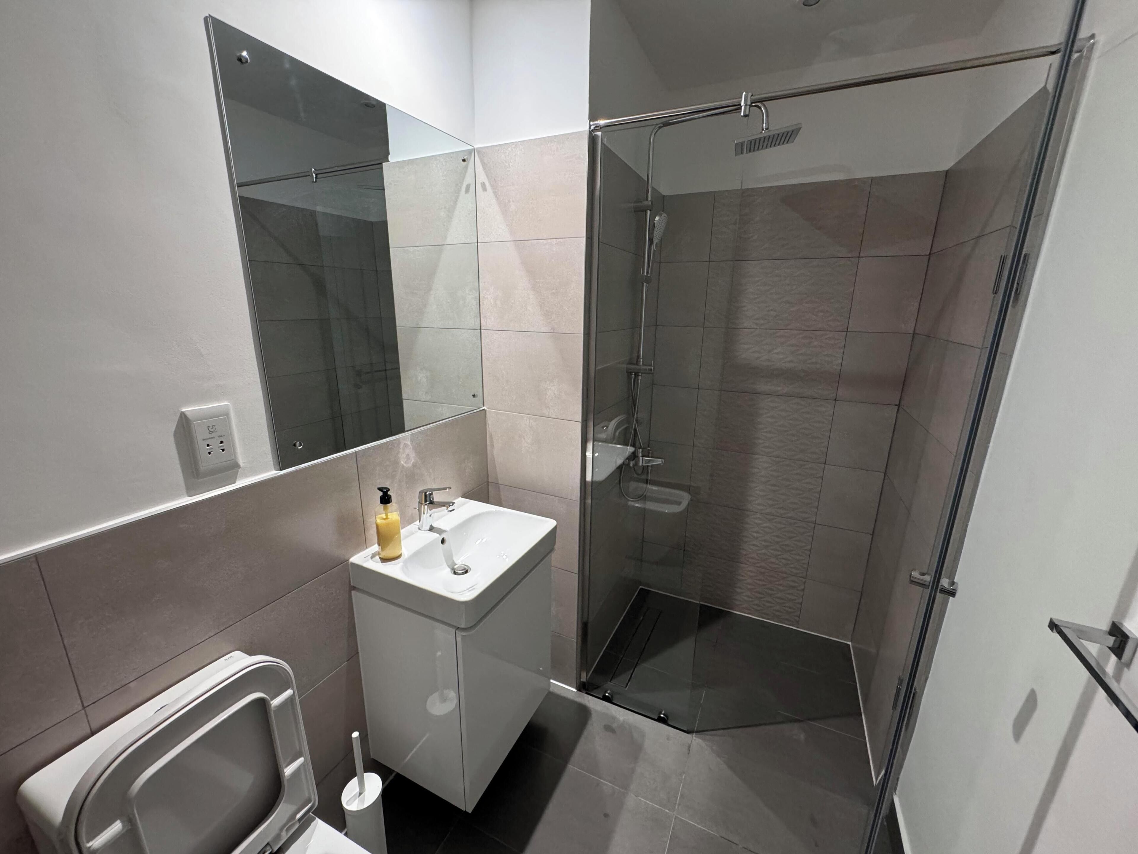 Un baño moderno con cabina de ducha de vidrio, un lavabo con espejo y un inodoro.