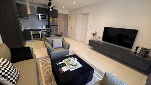 A modern living room with a sofa, a coffee table, a TV, and a kitchen in the background. - Loxwood Abode (Accra)