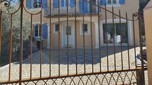 A two-story building with a balcony, a gated entrance, and a cobblestone driveway. - Villa Azur 6 bedrooms and heated pool 20 persons (Le Thoronet)