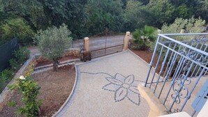 A paved pathway with a floral pattern leading to a gated entrance surrounded by trees and shrubs. - Villa Azur 6 bedrooms and heated pool 20 persons (Le Thoronet)
