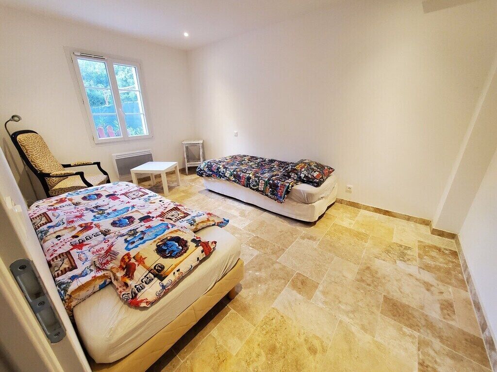 Ein Schlafzimmer mit zwei Betten, einem Sessel, einem kleinen Tisch und einem Fenster.