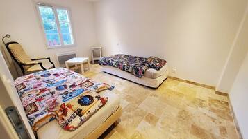 Ein Schlafzimmer mit zwei Betten, einem Sessel, einem kleinen Tisch und einem Fenster.