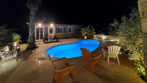 A swimming pool with chairs and a table, surrounded by plants and a building with lights. - Villa Azur 6 bedrooms and heated pool 20 persons (Le Thoronet)