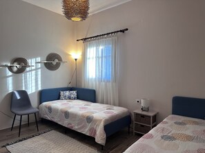 A bedroom with a bed, a chair, a bedside table, a lamp, and a window with curtains. - Genari Beach Apartments - Family sea View Apartment (Pyrgos)