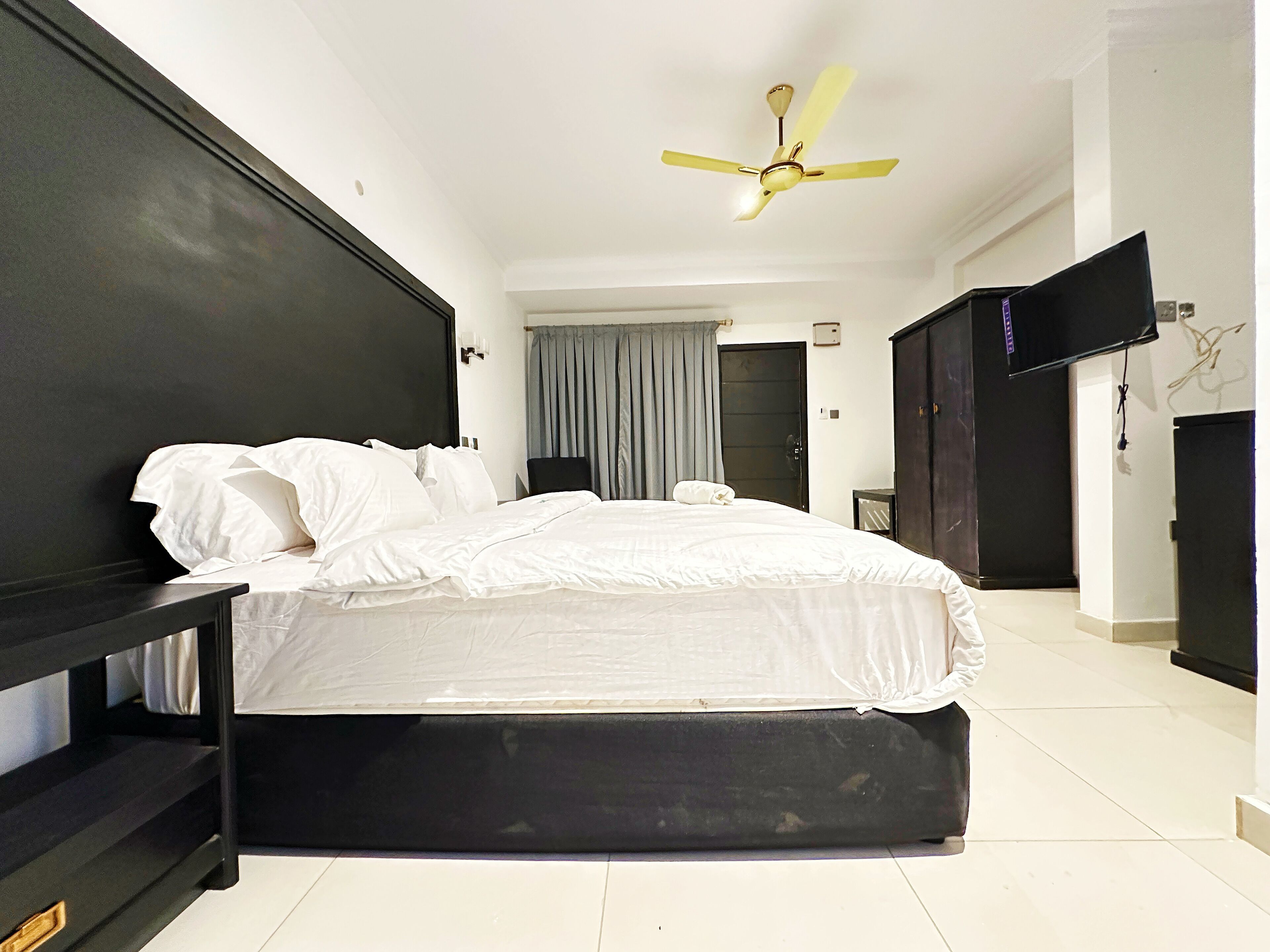 Een moderne hotelkamer met een groot bed, een plafondventilator, een televisie en een kledingkast.