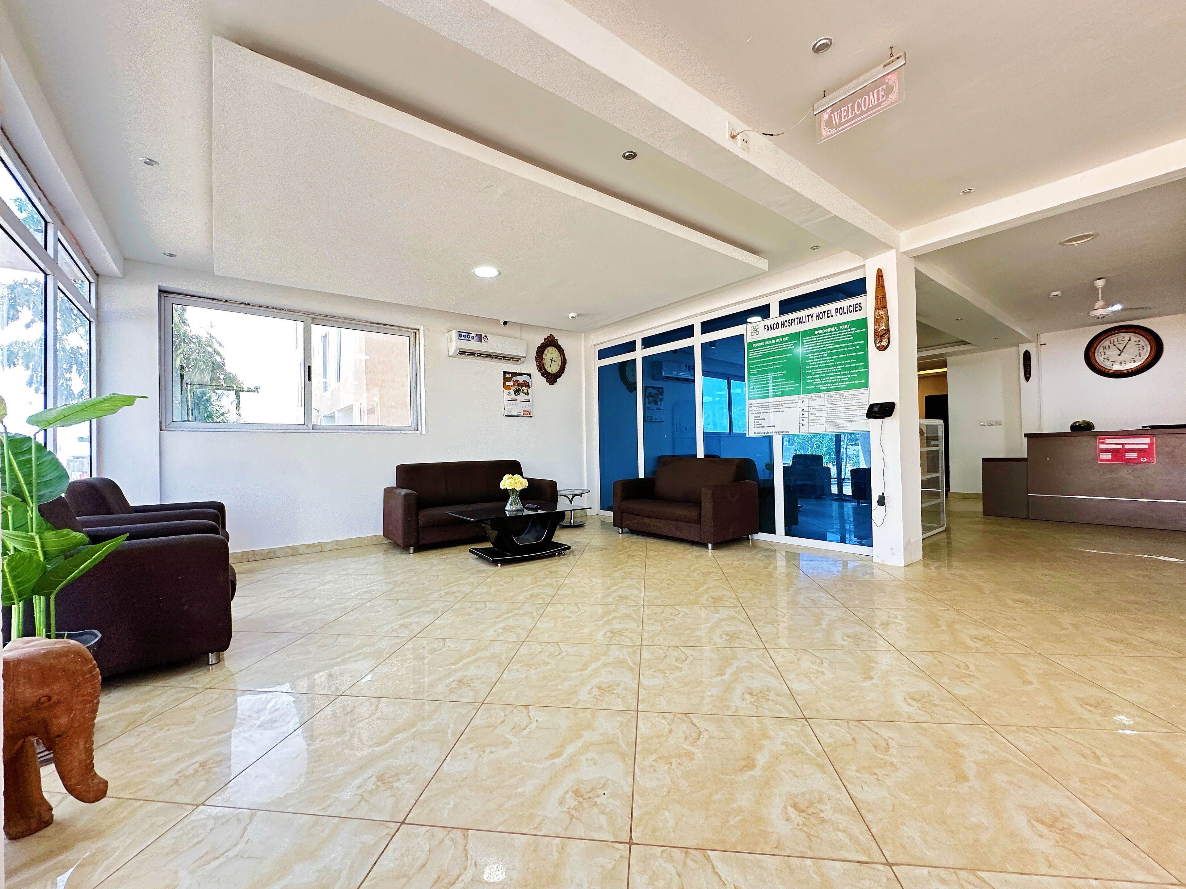 A hotel reception area with a reception desk, two sofas, a coffee table, and a large window providing natural light.