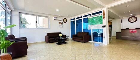 A hotel reception area with a reception desk, two sofas, a coffee table, and a large window providing natural light.
