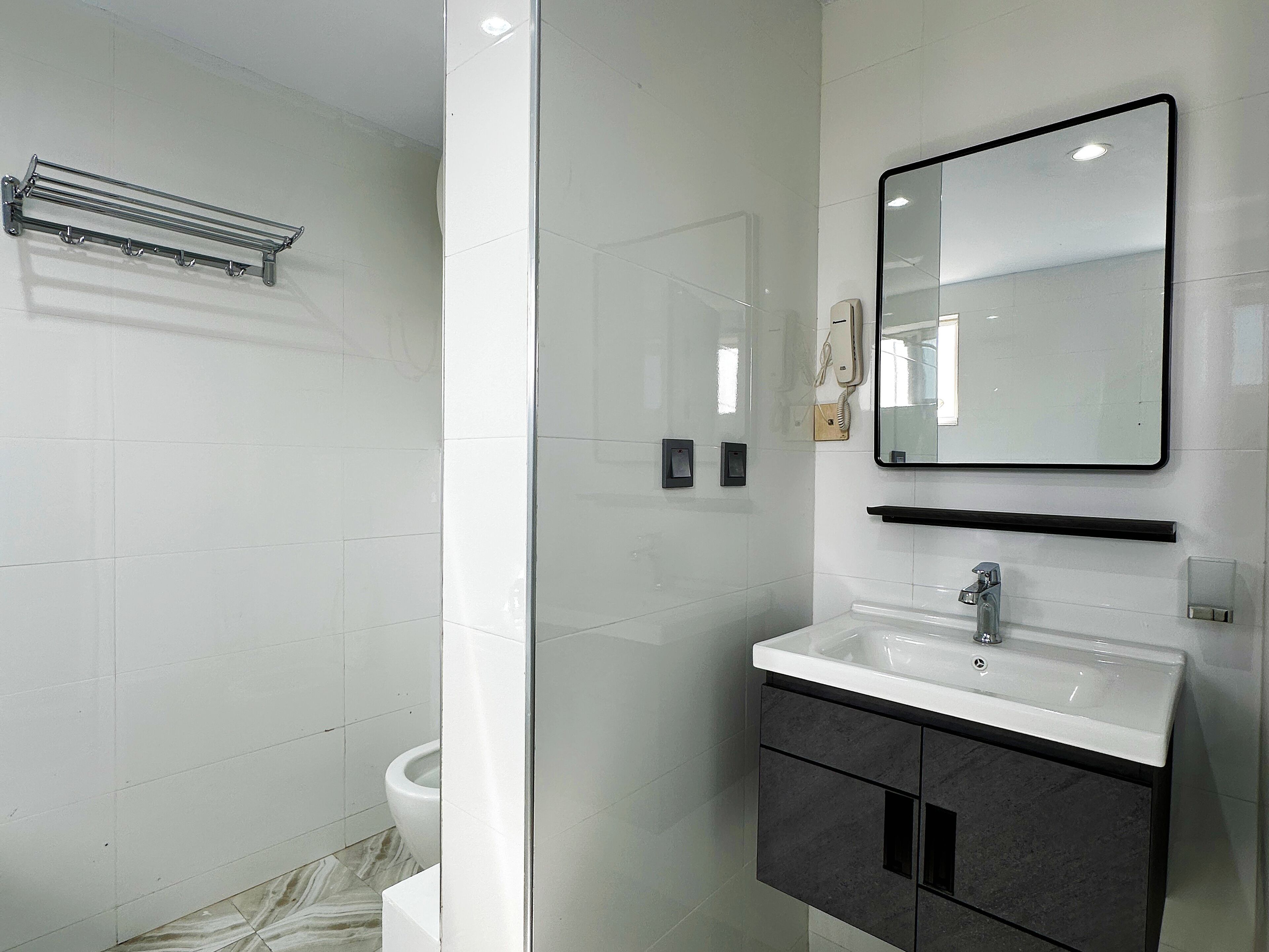 A modern bathroom with a glass shower enclosure, a white sink with a black cabinet, and a mirror above the sink.