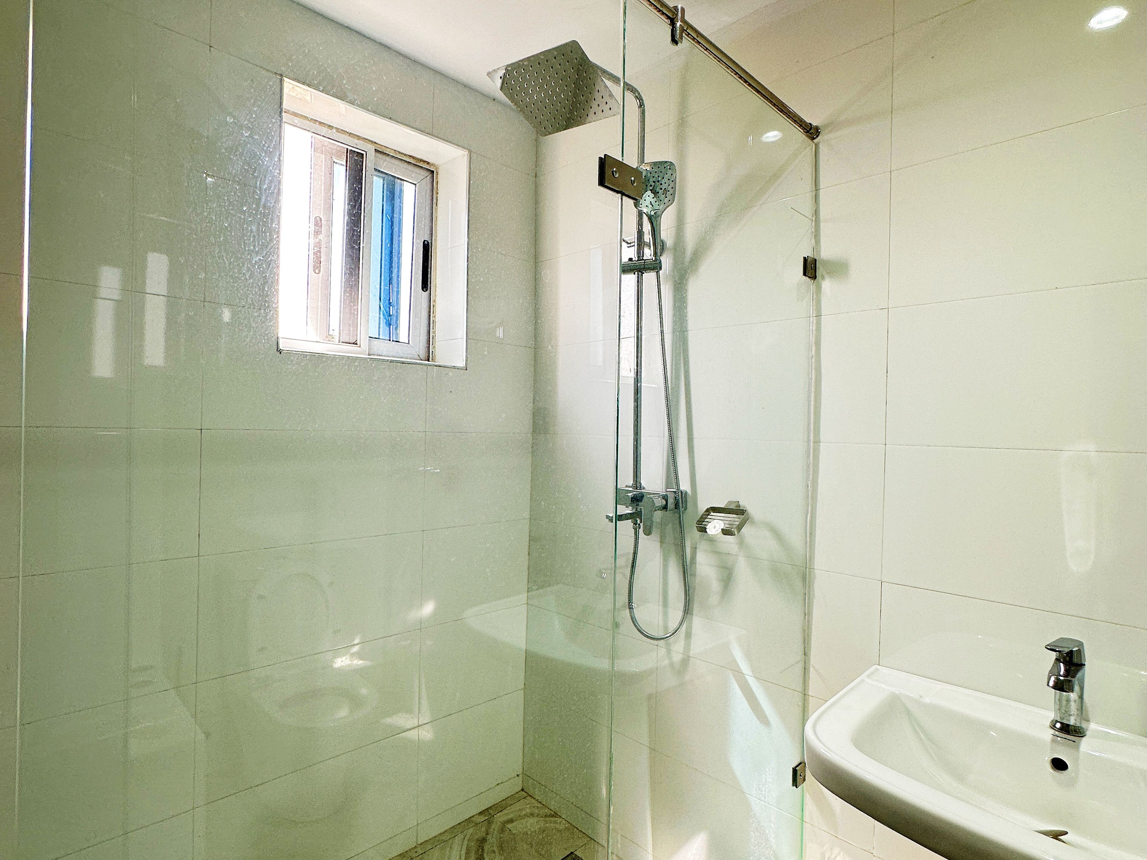 Ein Badezimmer mit einer gläsernen Dusche, einem Fenster mit blauen Vorhängen und einem weißen Waschbecken.