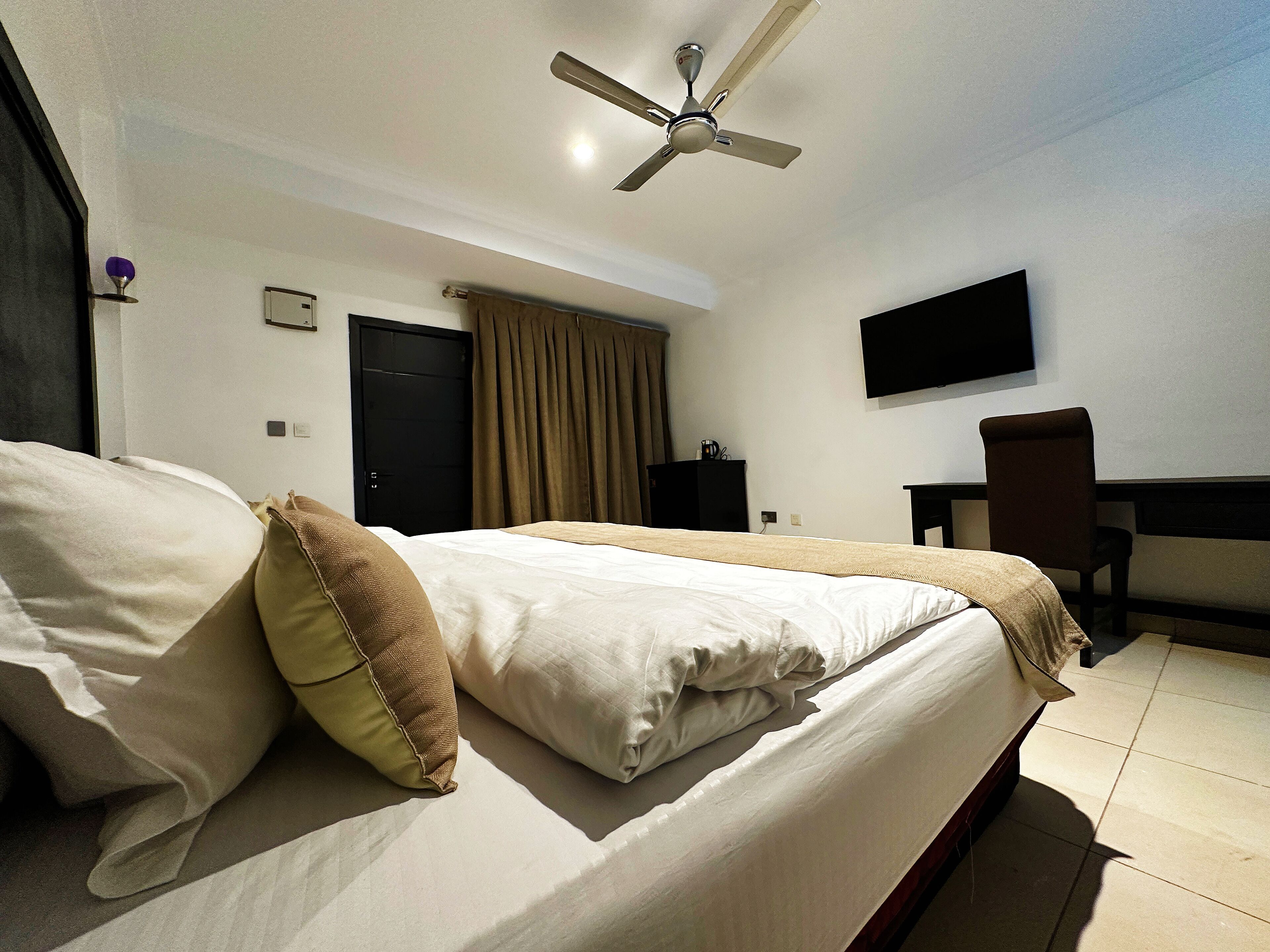 A hotel room with a bed, a desk, a chair, a TV, and a ceiling fan.