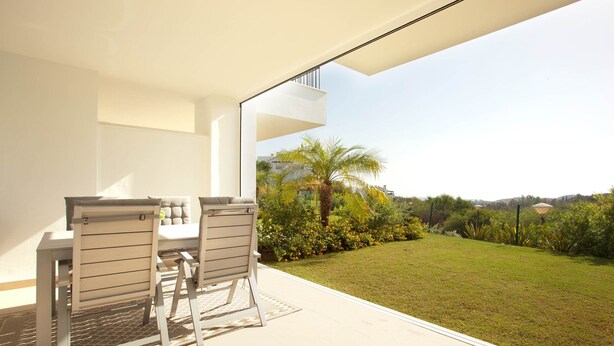 A modern outdoor patio with a table and chairs, a clear view of a lush garden and distant hills. - Ojen Apartment Near Golf (Ojén)