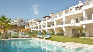 A swimming pool with lounge chairs and a grassy area, surrounded by multi-story buildings with balconies. - Ojen Apartment Near Golf (Ojén)