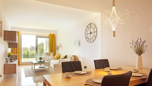 A modern dining area with a wooden table set for four, a large wall clock, and a decorative light fixture. - Ojen Apartment Near Golf (Ojén)
