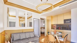 Een moderne woonkamer met een grijze bank, een eettafel met stoelen, en een keuken met kasten en apparatuur.