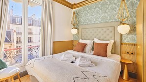 Een hotelkamer met een groot bed, een balkon met uitzicht op Parijse gebouwen, en een klassiek design met gouden accenten.