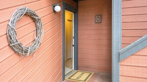 Une façade en bois ornée d’une guirlande, d’un paillasson et d’une porte sur laquelle est apposé un numéro.