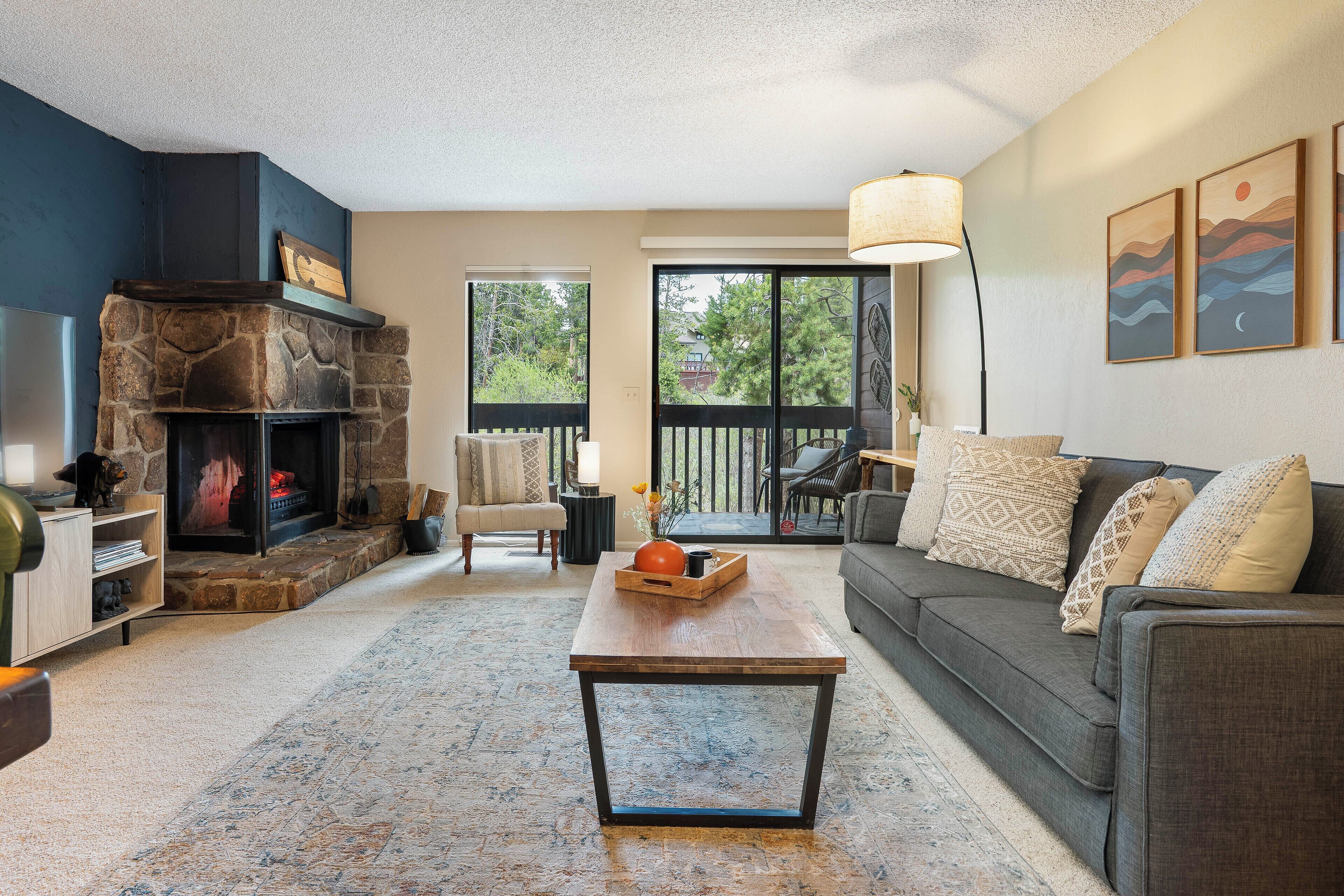 A living room with a stone fireplace, a sofa, a coffee table, and a large window.