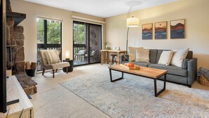 A living room with a sofa, coffee table, and a stone fireplace. - 6 Mi to Skiing: Condo w/ Balcony in Fraser! (Fraser)