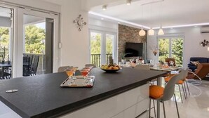 A modern kitchen with a central island, bar stools, a dining area, and a TV mounted on the wall. - Modern & Stylish Villa With Private Pool (Omis)