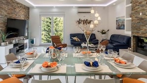 A modern dining room with a glass table set for a meal, surrounded by comfortable seating and a television. - Modern & Stylish Villa With Private Pool (Omis)