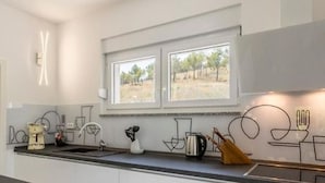 A modern kitchen with white cabinets, a black countertop, and a window overlooking a natural landscape. - Modern & Stylish Villa With Private Pool (Omis)