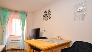 Une pièce avec une table en bois, deux chaises noires, un téléviseur et une horloge murale décorative.