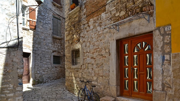 Une ruelle étroite pavée, avec un vélo garé devant un bâtiment en pierre doté d’une porte et de fenêtres en bois.