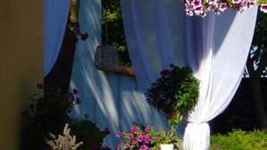 Un jardin agrémenté de rideaux blancs, d’une suspension florale et de différentes plantes en pot.