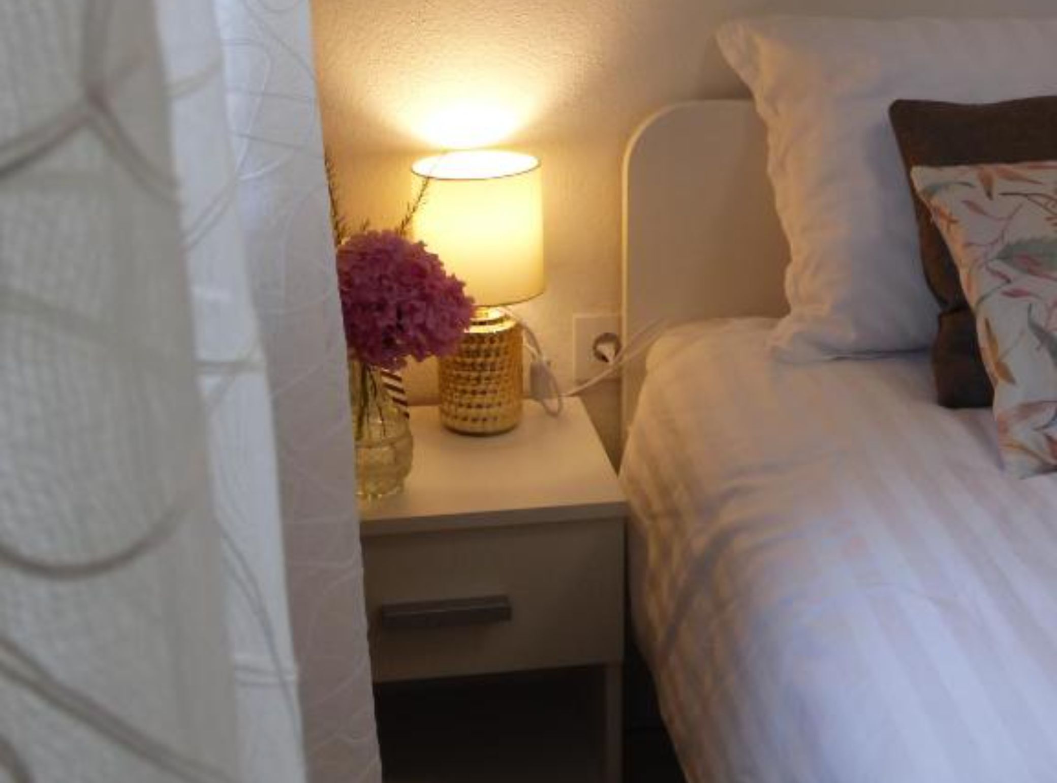 A hotel room with a bed, a nightstand, a lamp, and a vase with flowers.