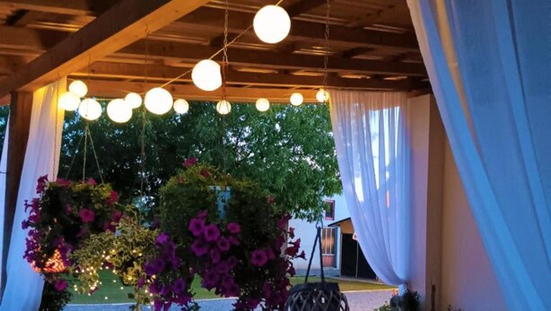 Un espace extérieur aménagé pour les repas, agrémenté de suspensions florales et de guirlandes lumineuses.