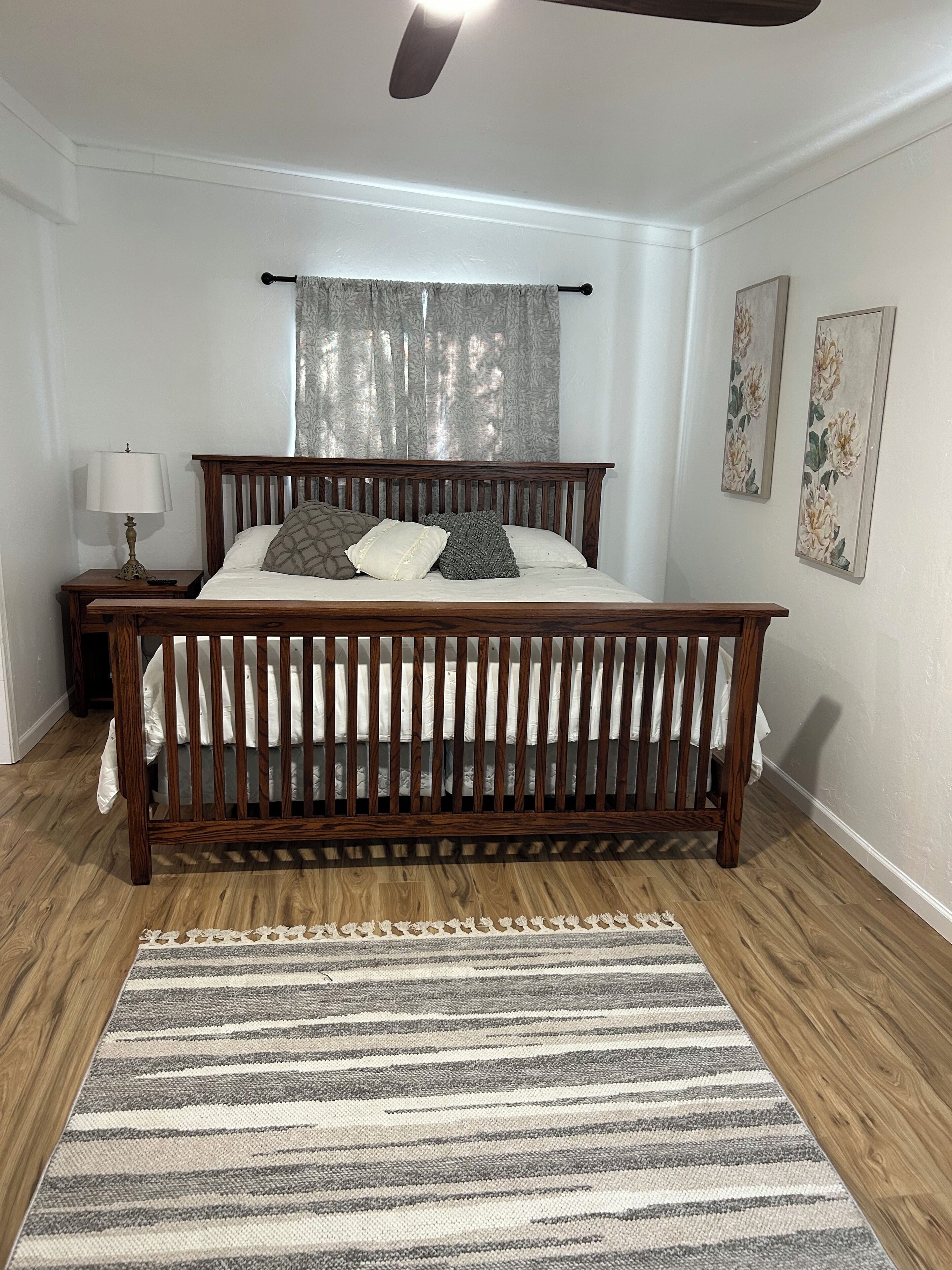 Un dormitorio con una cama de madera, una mesita de noche con lámpara, un tapete a rayas y decoración floral en la pared.