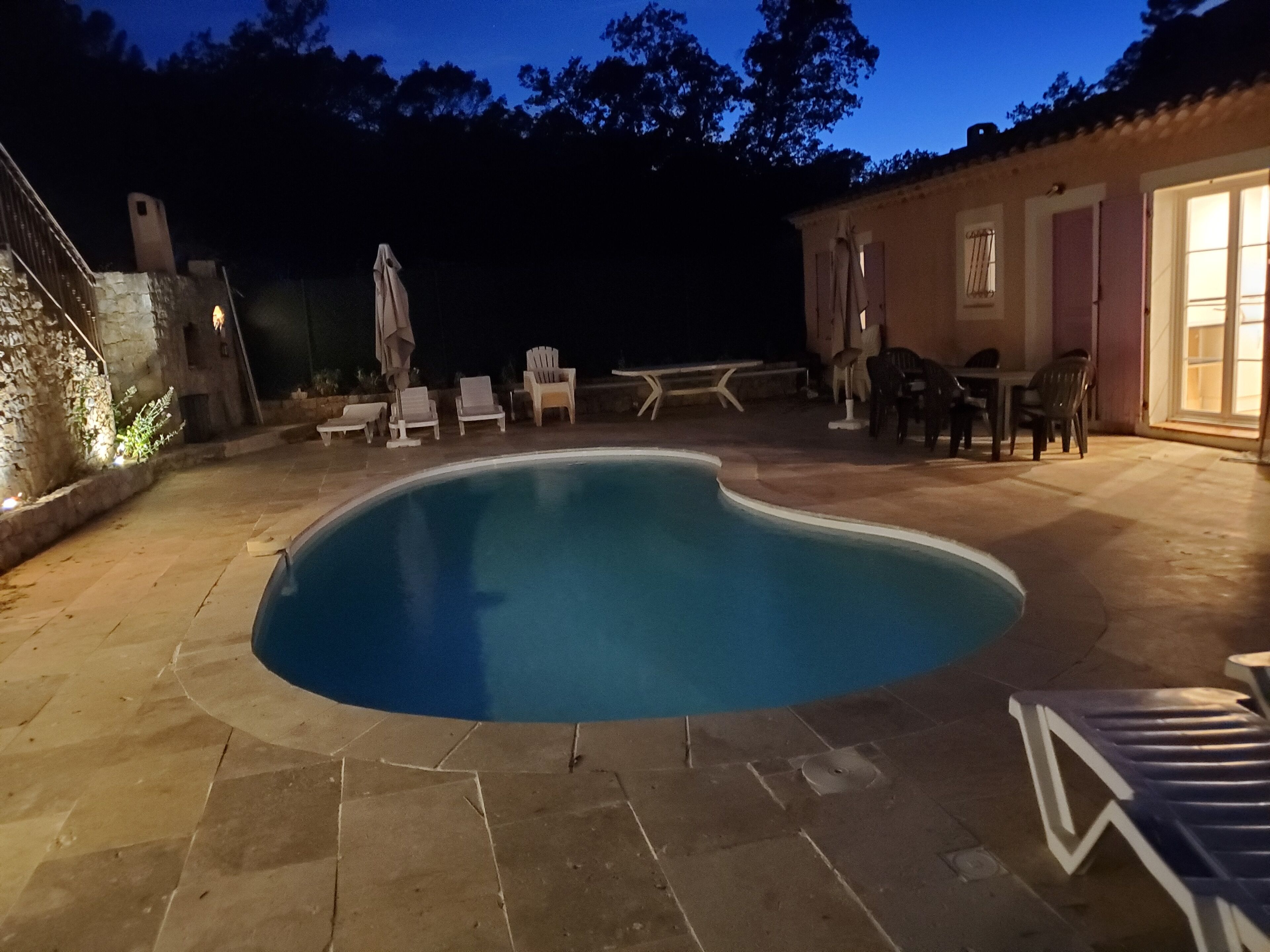 A swimming pool with a stone deck, surrounded by lounge chairs and a patio table.