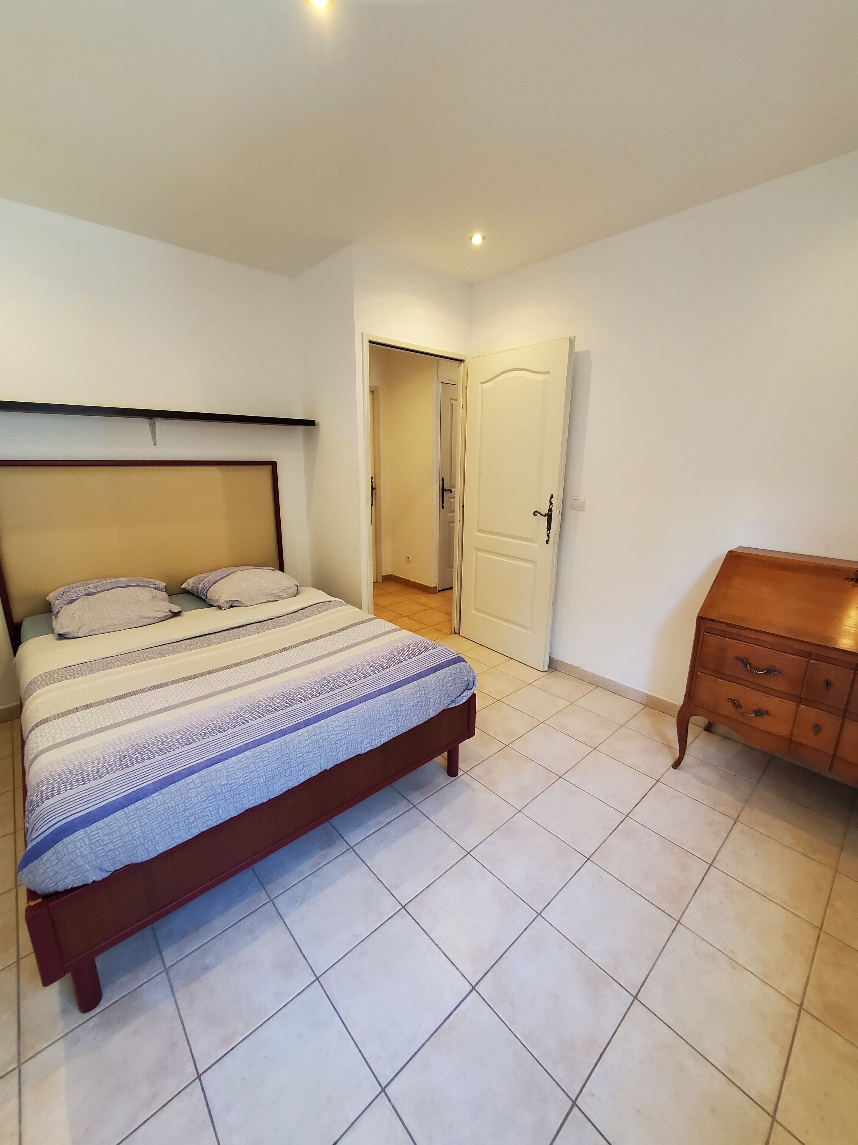 A bedroom with a bed, a wooden dresser, and a door leading to another room.