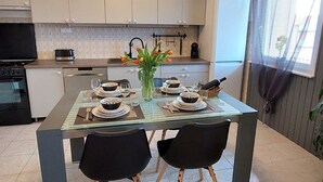 A modern kitchen with white cabinets, a dining table set for four, and a vase of tulips. - Modern Crikvenica Apartments With Sea View (Crikvenica)