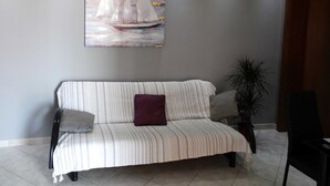 En stribet sofa med en lilla pude, en potteplante og et maleri af sejlbåde på væggen.