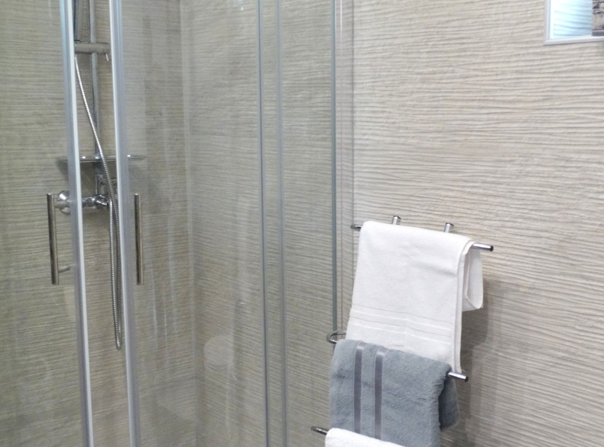 A glass-enclosed shower stall with a towel rack holding two towels.