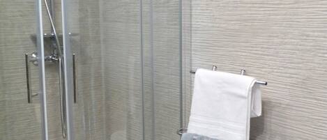 A glass-enclosed shower stall with a towel rack holding two towels.